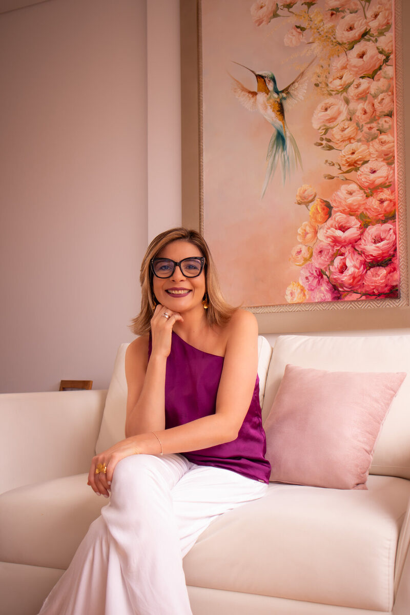 Fabiola Quintero sonríe sentada en el sofá crema de su consulta, bajo un cuadro de flores rosas.